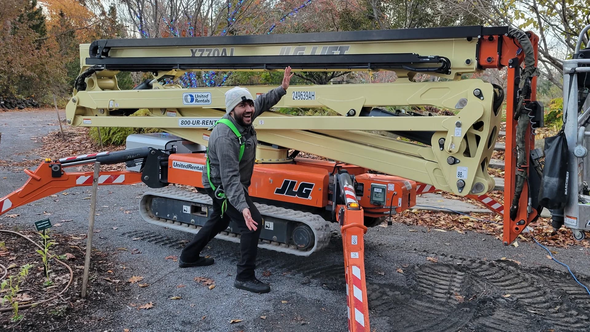 Me in a safety harness in front of the JLG compact crawler boom lift used for tree-canopy projector rigging.